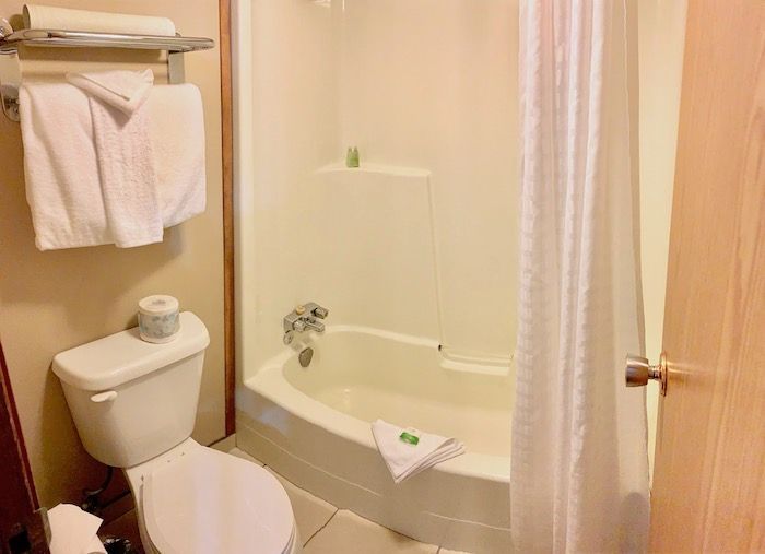 Bathroom with a white toilet, bathtub, and towels. The walls are light brown and cream-colored.