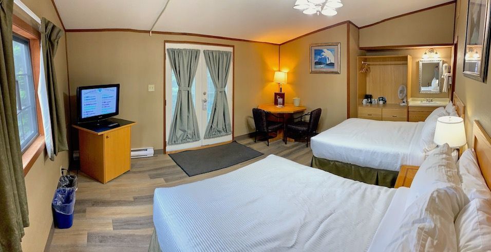 Motel room with two beds, small table, TV, window, and closed double doors.