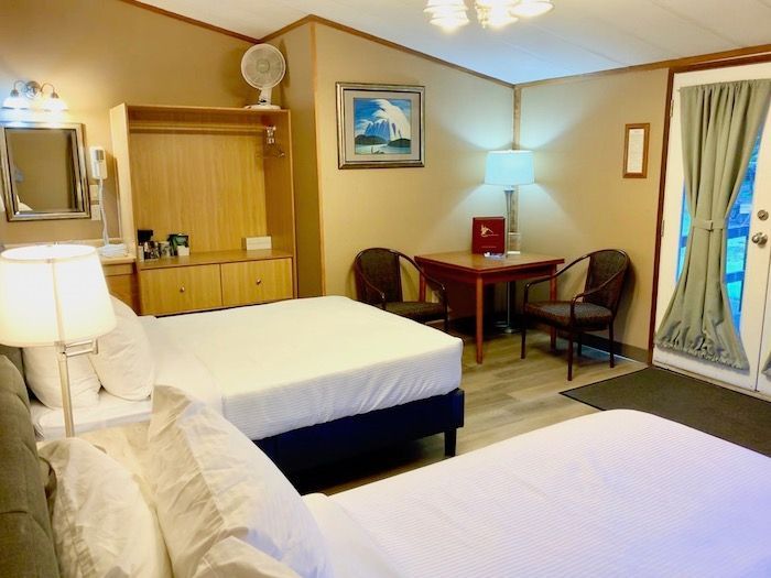 Hotel room with two beds, small table, and a door to the outside.