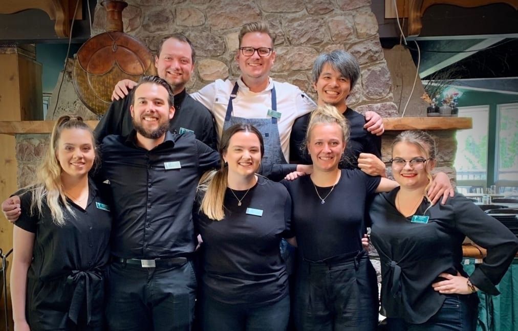 Restaurant staff posing together, some with arms around each other. Inside with stone wall.