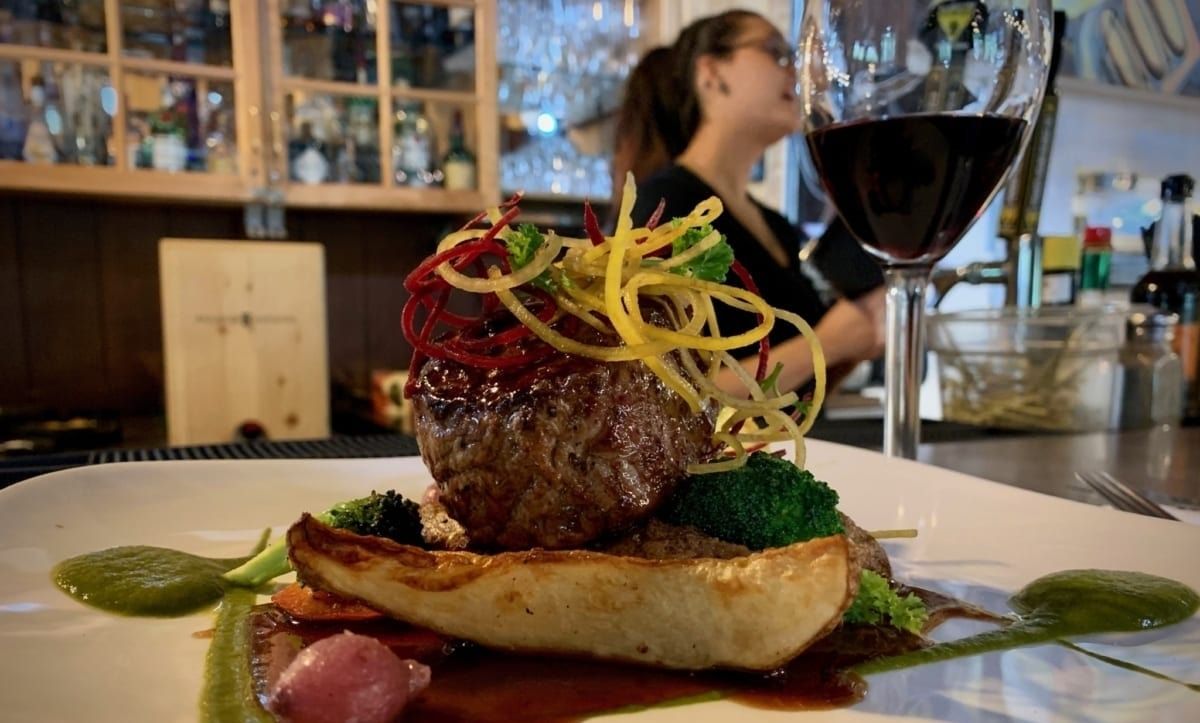 Gourmet dish on plate with wine glass, bartender in background.