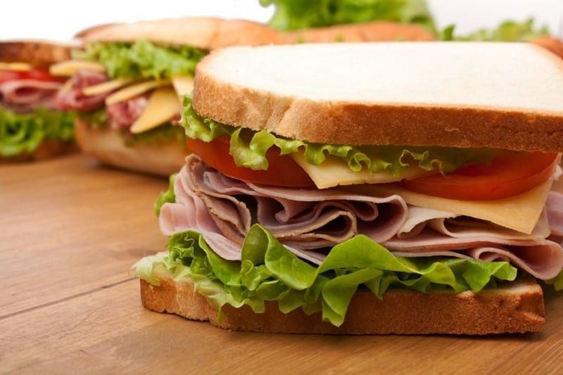 Sandwiches with ham, cheese, lettuce, and tomato on white bread, on a wooden surface.