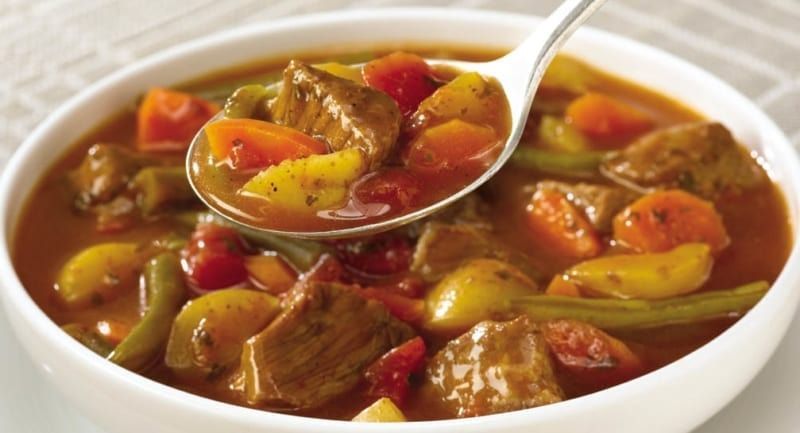 Beef stew in a white bowl, a spoonful being lifted up; carrots, potatoes, and green beans are visible.