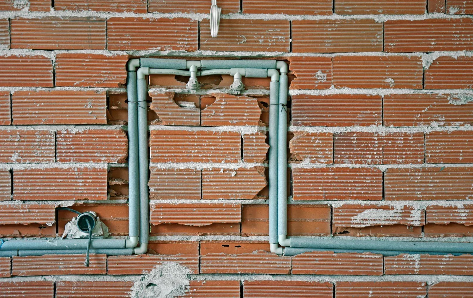 Red brick wall with exposed plumbing pipes forming a rectangular frame.