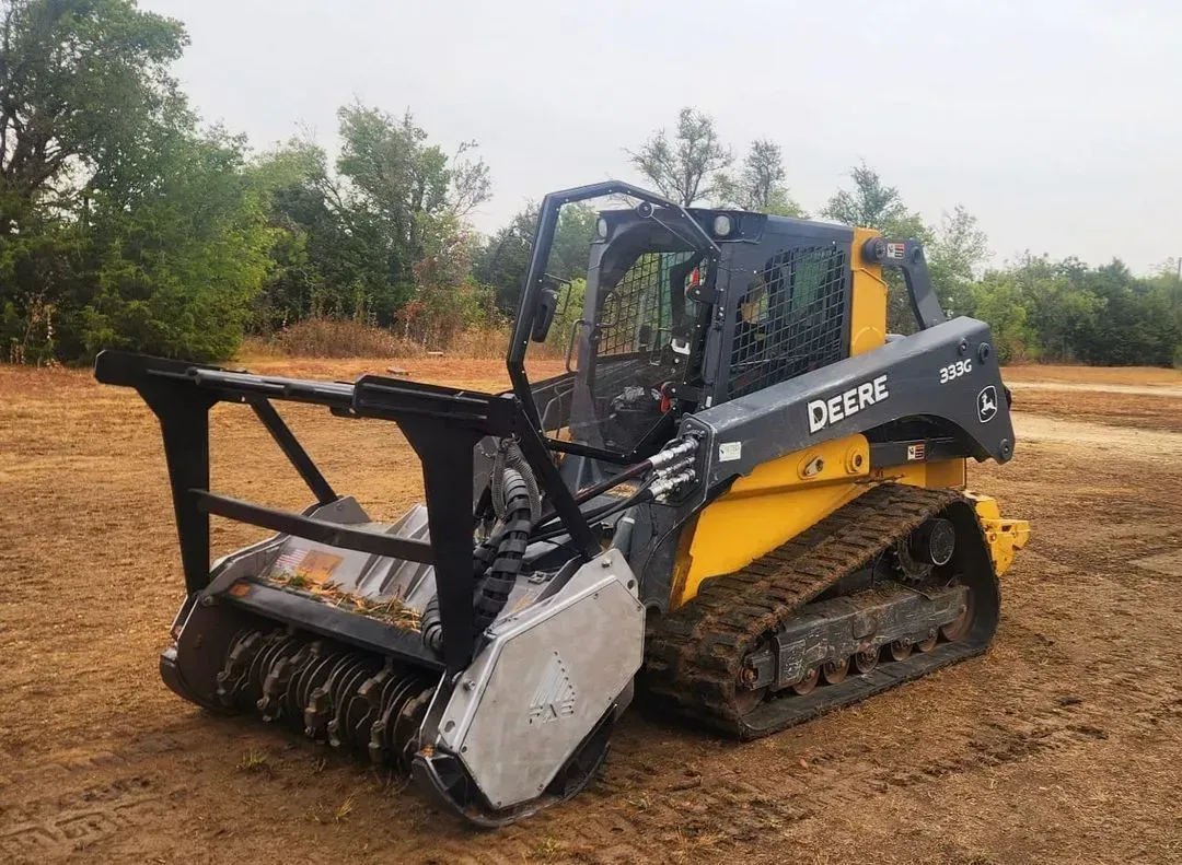 Yellow and black John Deere skid steer with forestry mulcher attachment in a field.