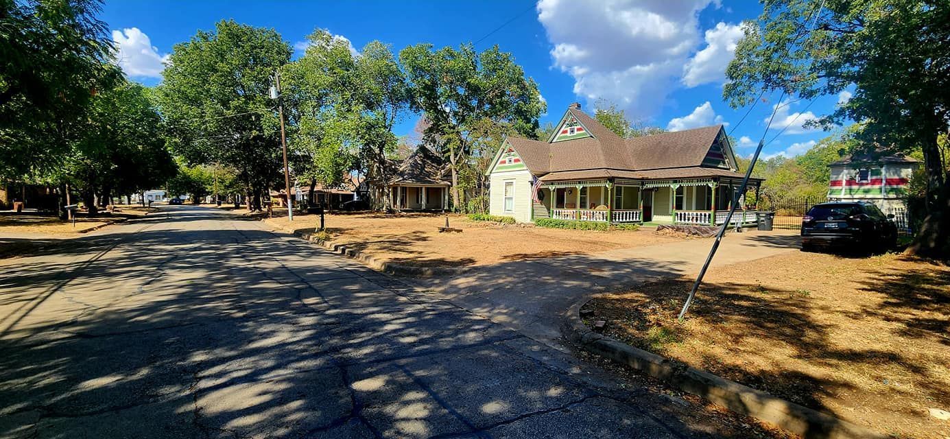 Street view of houses under a bright blue sky with trees and shadows.