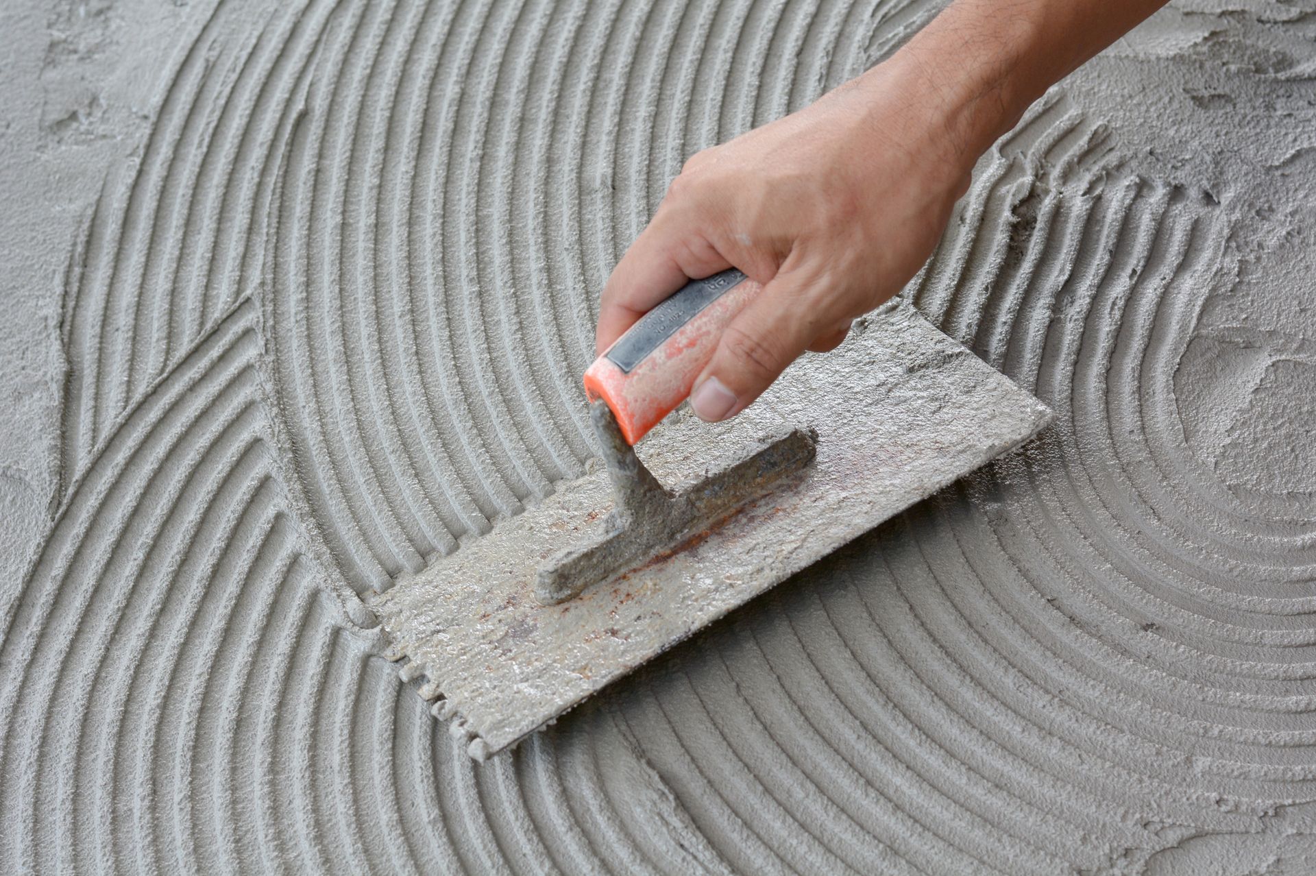 A Person Is Spreading Adhesive on A Tile Floor with A Trowel | Saint Cloud, WI | Feldner Construction Inc.
