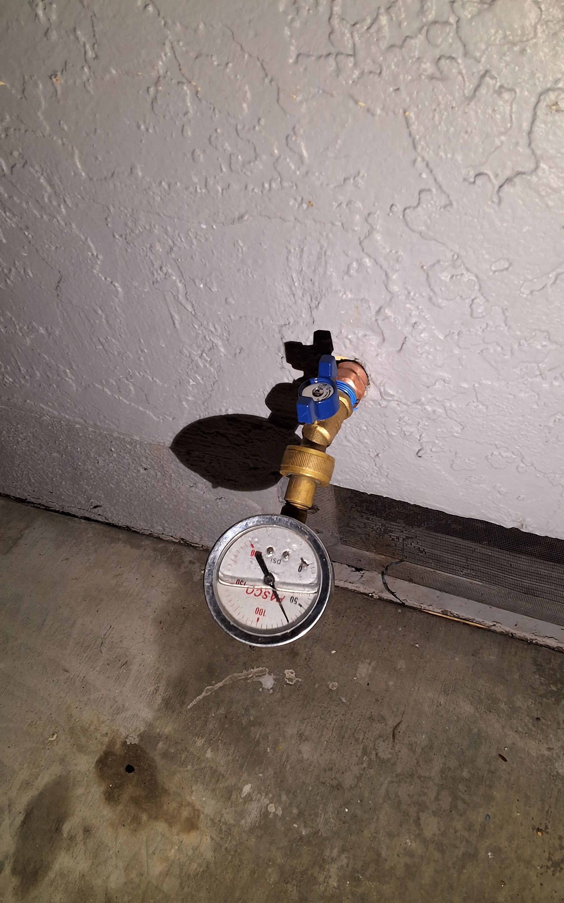 A pressure gauge is attached to a faucet on a wall.