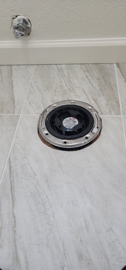 A toilet flange is sitting on a tiled floor in a bathroom.