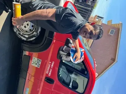 A man is standing next to a red van holding a drink.