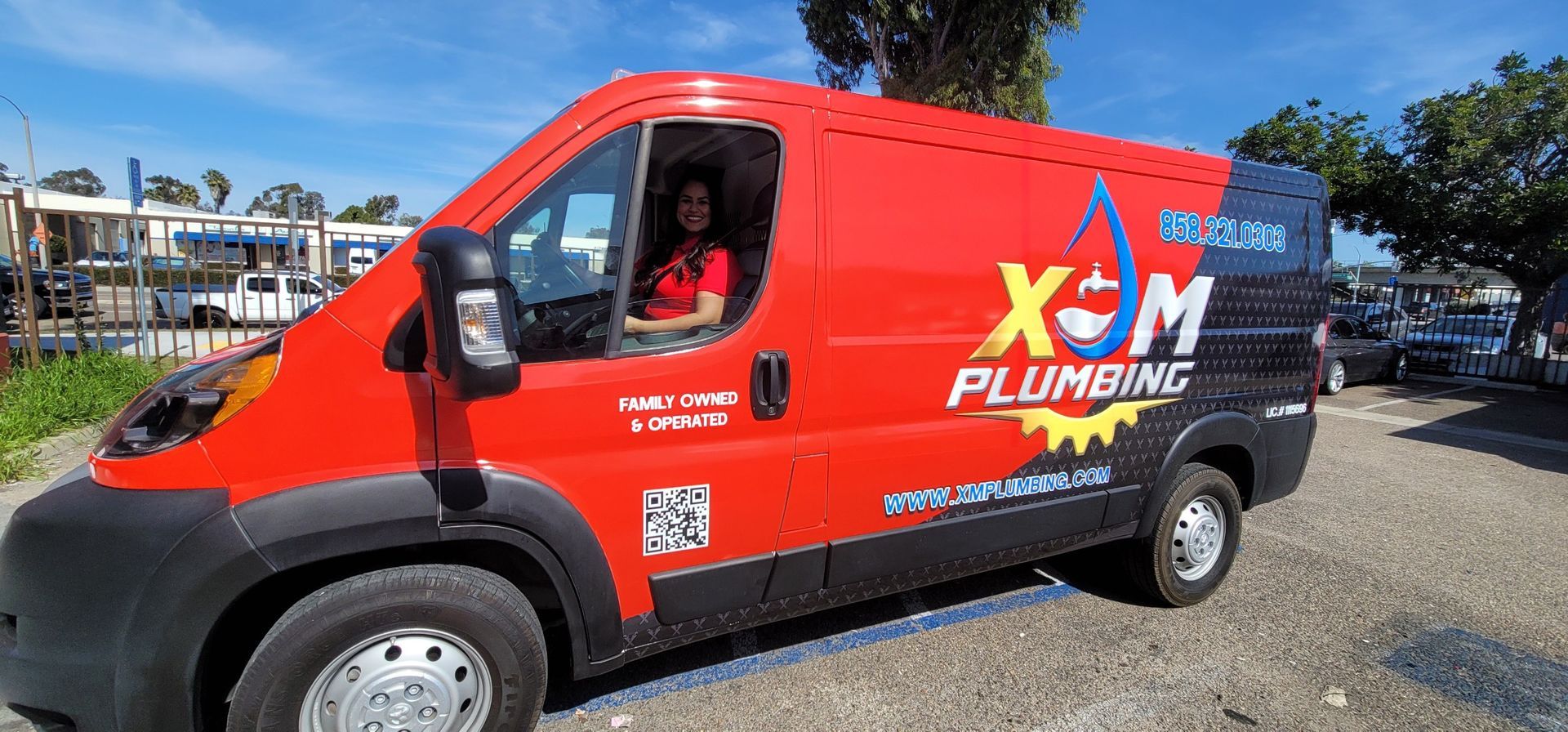 A red van with the word plumbing on it is parked in a parking lot.