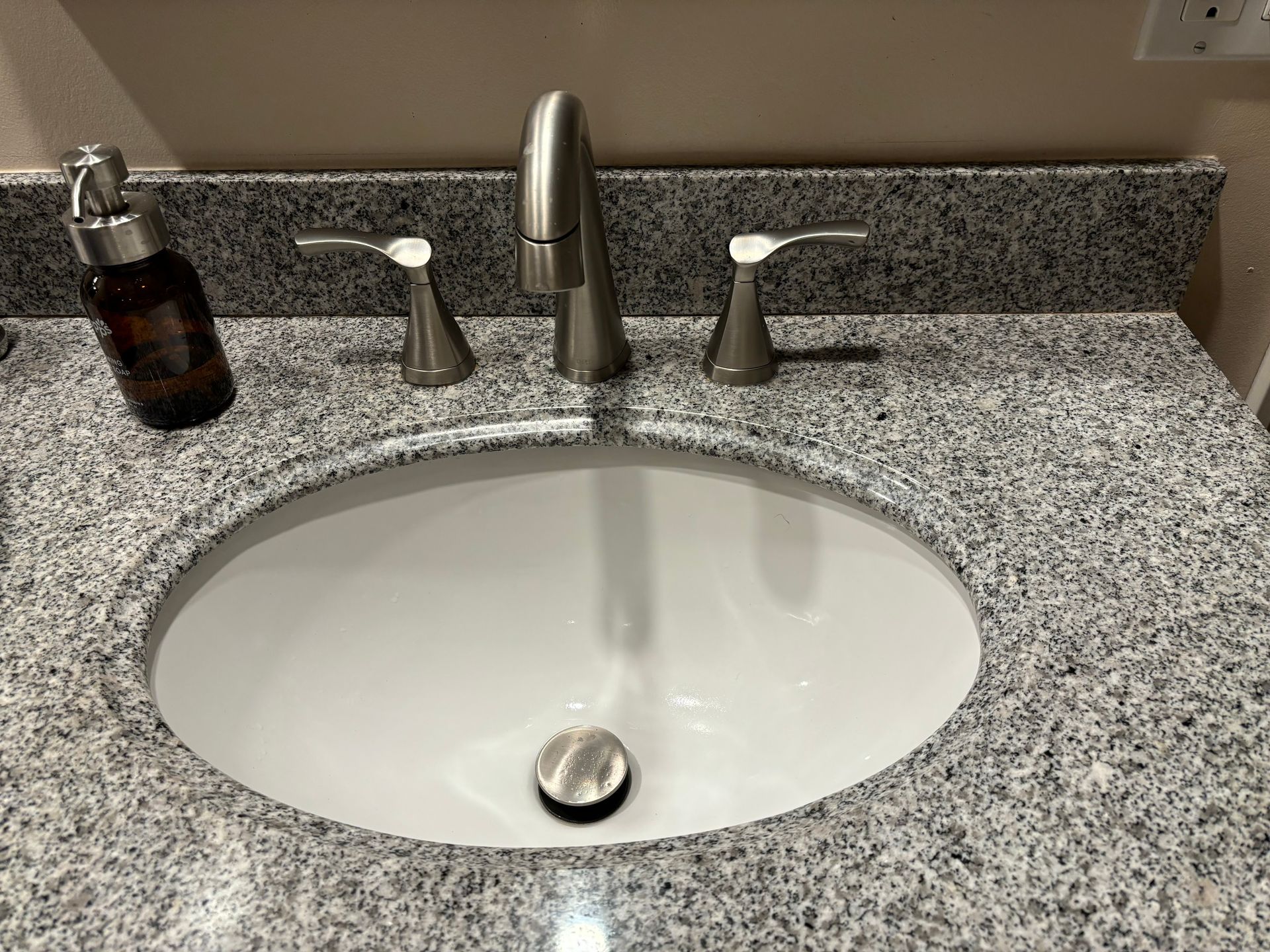 A bathroom sink with a faucet and soap dispenser on a granite counter top.