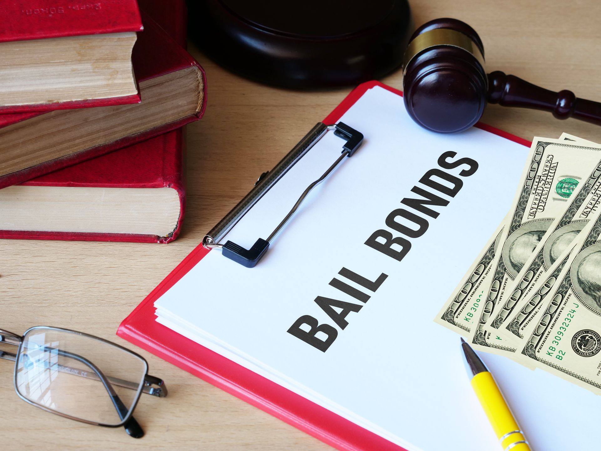 Clipboard labeled “Bail Bonds” with cash, gavel, glasses, and books on a desk