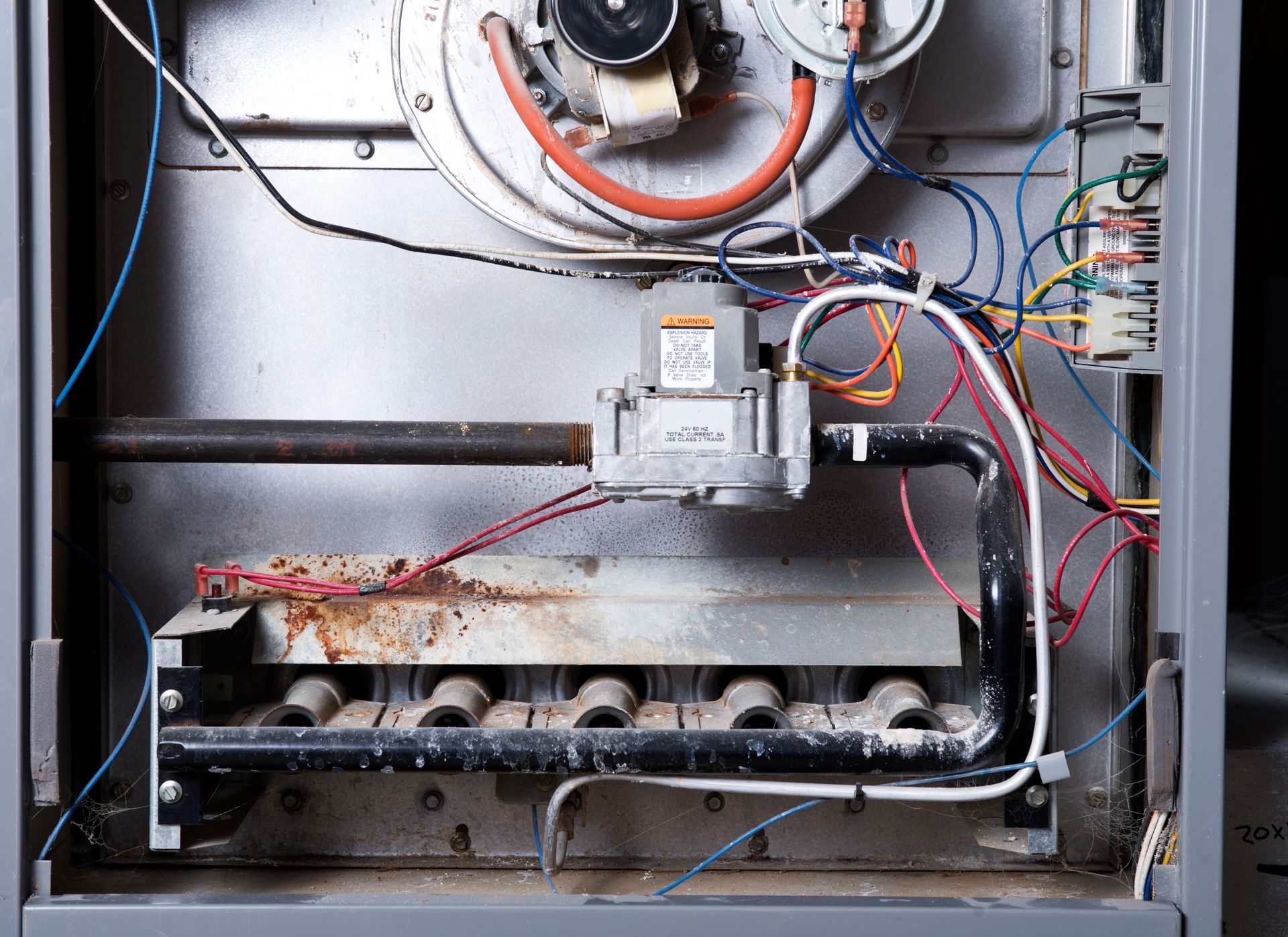 Interior view of a furnace showing burners, gas valve, wiring, and metal components. Interior view of a furnace showing burners, gas valve, wiring, and metal components.