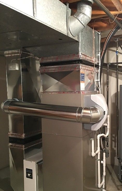 Metal HVAC ductwork with rectangular and cylindrical components against a light-colored wall. Metal HVAC ductwork with rectangular and cylindrical components against a light-colored wall.