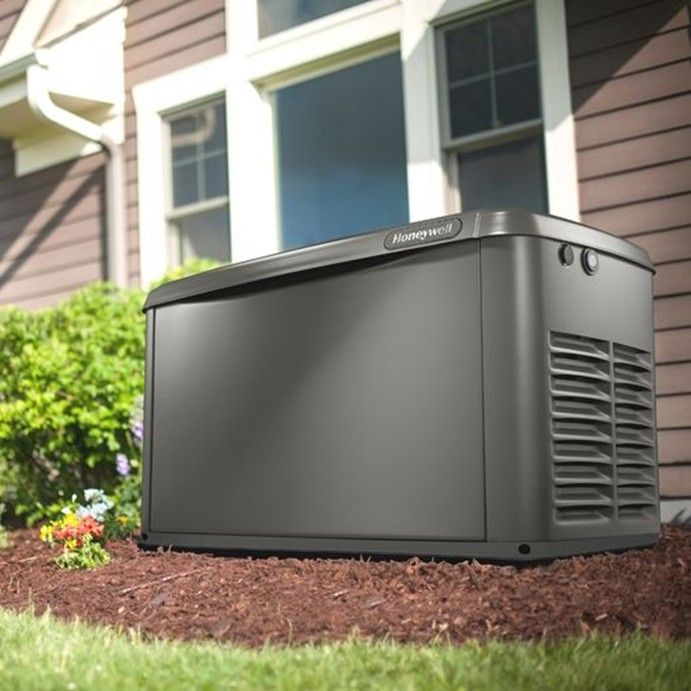 A dark grey Honeywell standby home generator sitting on a mulch bed next to the side of a house. A dark grey Honeywell standby home generator sitting on a mulch bed next to the side of a house.