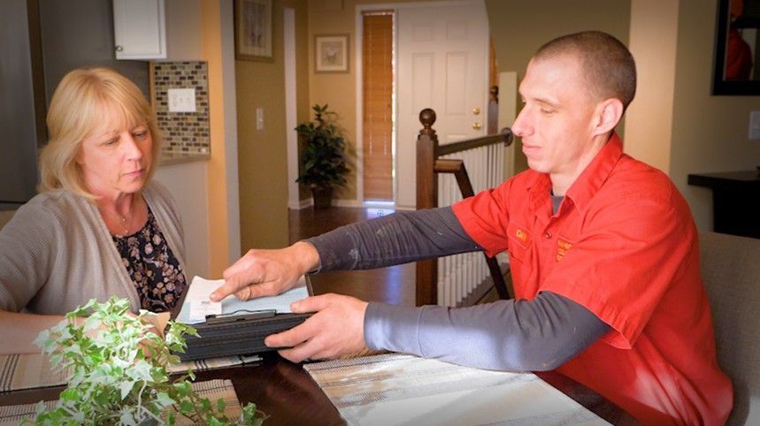 Two people at a table sorting papers in a home office, with a printer and plants nearby. Two people at a table sorting papers in a home office, with a printer and plants nearby.