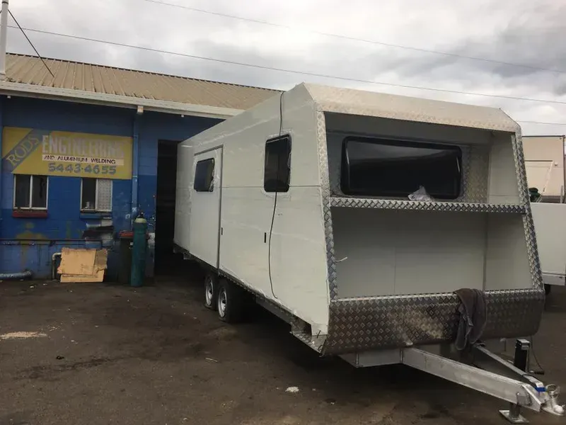 White Travel Trailer on a Trailer Hitch Outside a Blue Building — Rod's Engineering & Lifetime Trailers in Bli Bli, QLD