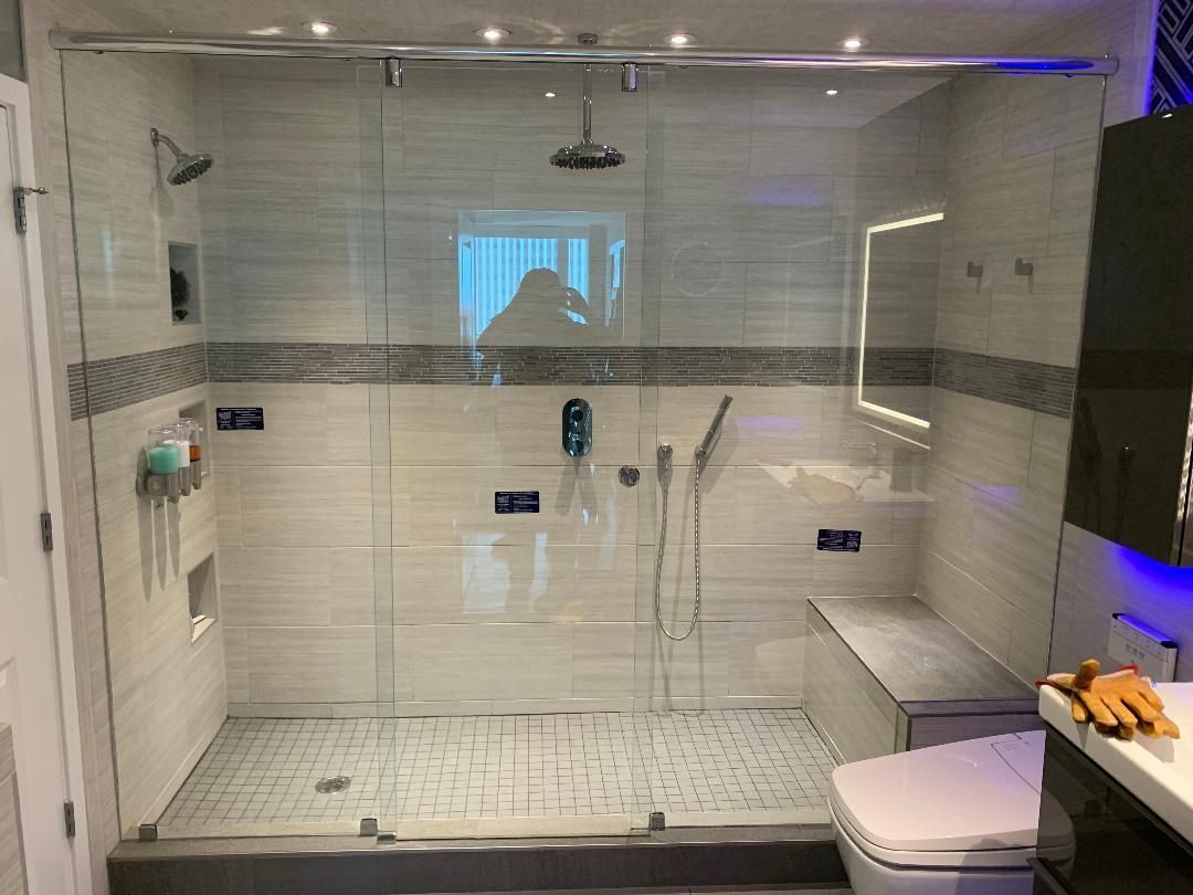 Modern bathroom with a glass shower, white and gray tiles, built-in bench, and a lighted mirror.