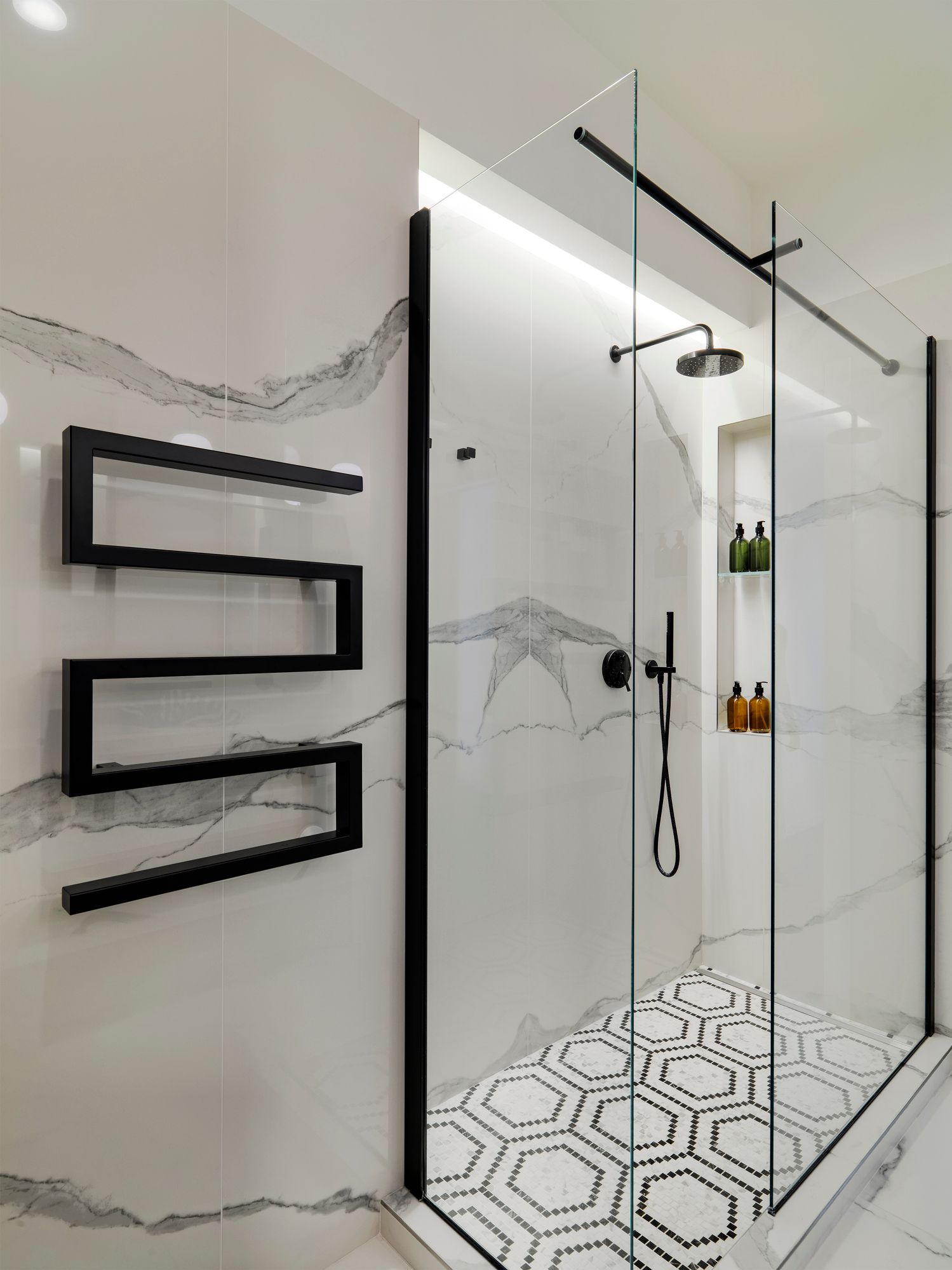 Modern bathroom with frameless glass shower doors featuring black hardware and marble walls.