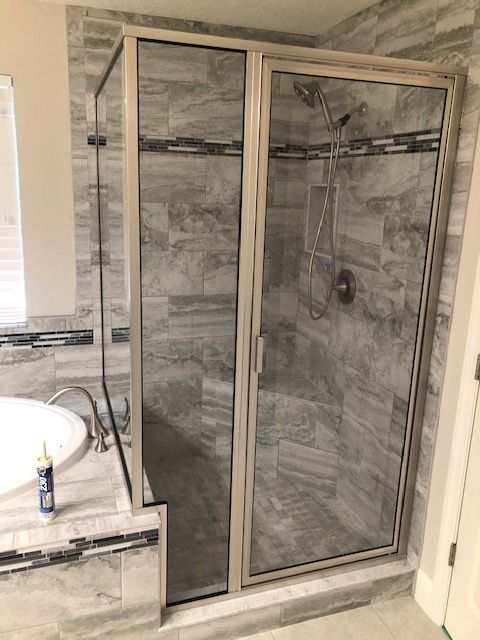 Shower with glass doors and silver frame, set in bathroom with gray tile.