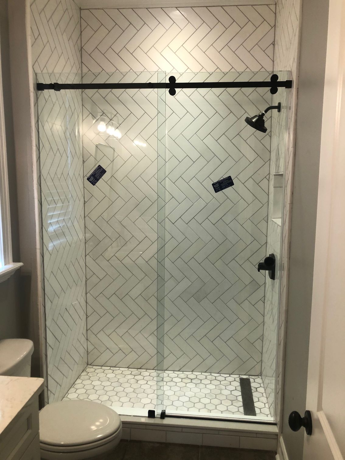 Modern bathroom with herringbone tile, glass shower, and black fixtures.
