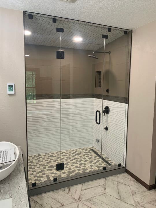Glass shower enclosure with black hardware, white and textured tile, and pebble floor.