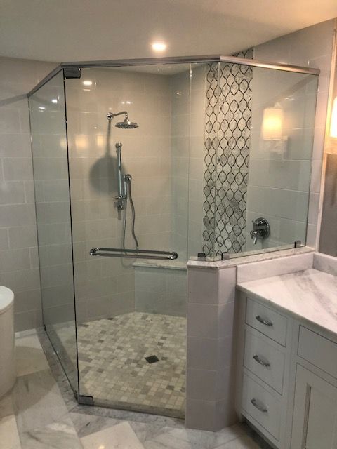 Glass-walled shower with white and gray tile, pebble floor, and white vanity.