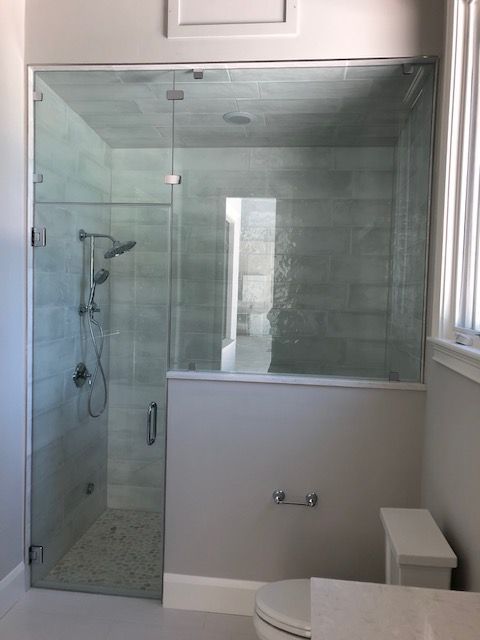 Glass shower enclosure with gray tiled walls. The toilet is to the right.