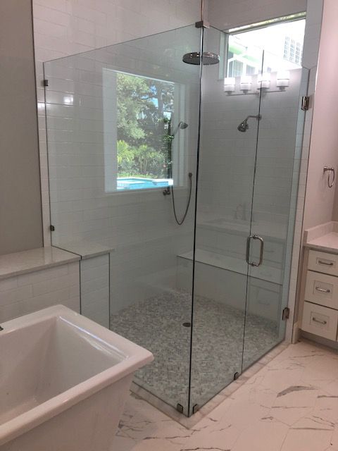 Glass shower enclosure with white tile and pebble floor, next to a white bathtub.