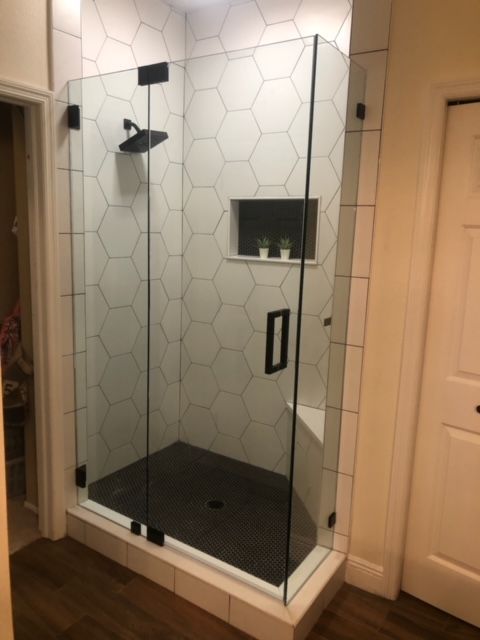 Modern bathroom with glass shower enclosure, black fixtures, and patterned white tiles.