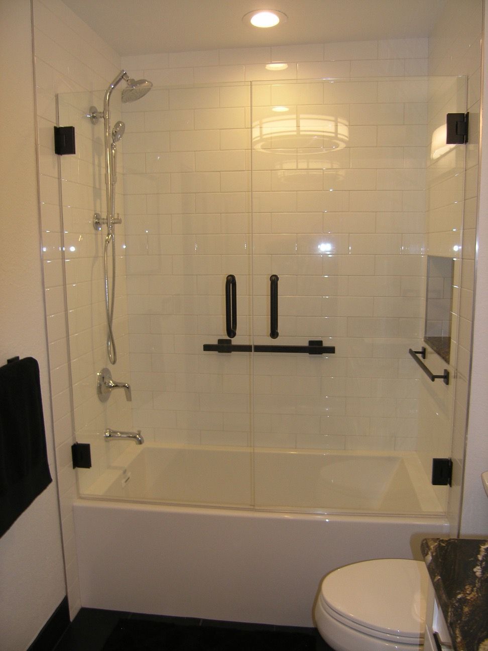 Bathroom with glass shower doors over a white bathtub, black hardware, and white subway tile.
