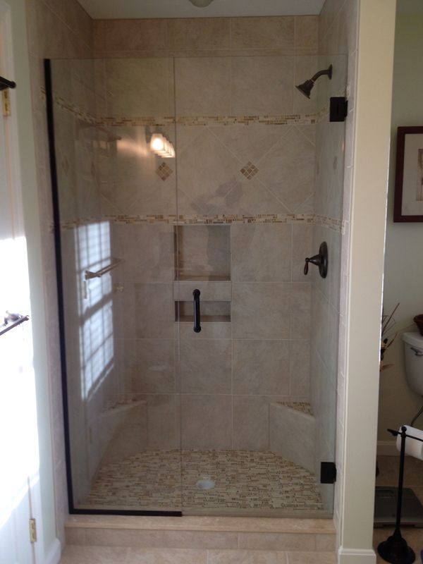 Glass shower enclosure with black hardware, beige tiled walls, and pebble flooring.