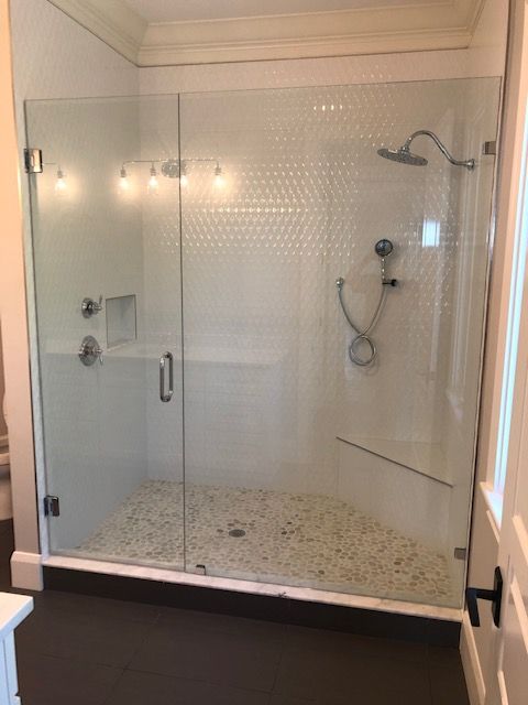 Glass shower with white hexagon tile and pebble floor.
