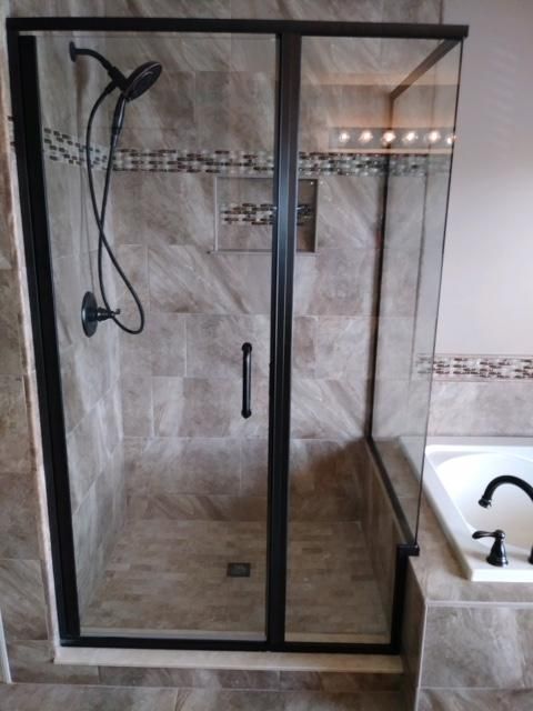 Black-framed glass shower enclosure with dark fixtures and light brown tiled walls.