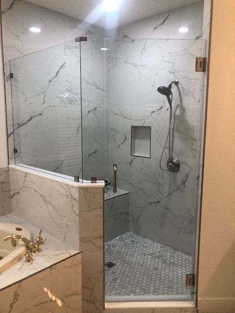 Glass-enclosed shower with white marble-look tile, brushed bronze hardware, and a built-in bench.