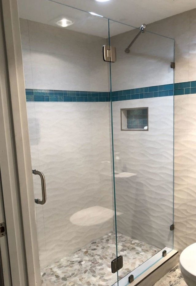 Glass shower enclosure with white wavy tile, teal accent, and pebble floor.
