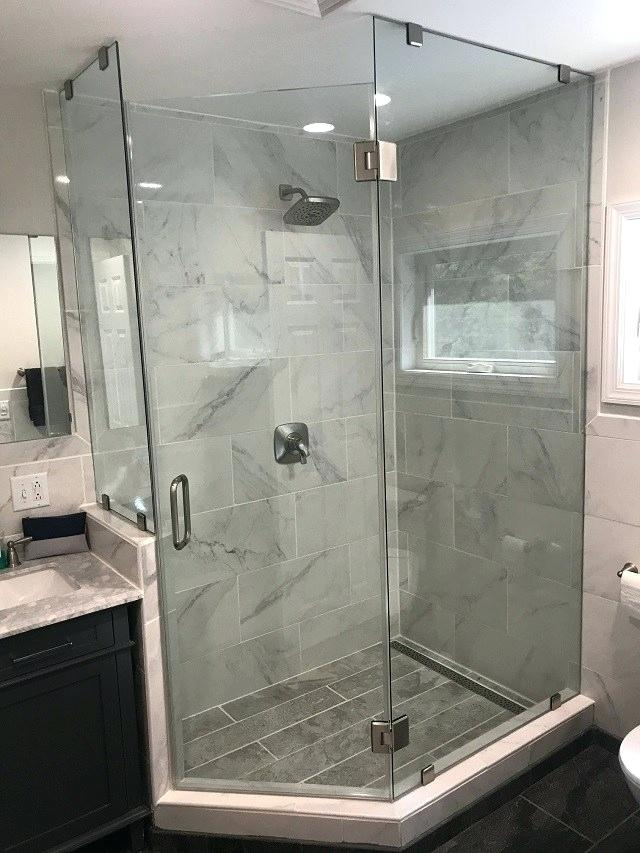 Glass shower enclosure in a bathroom with gray tile walls and flooring, chrome fixtures.