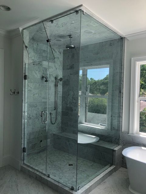 Glass shower enclosure in a bathroom with a window, marble walls, and a built-in bench.