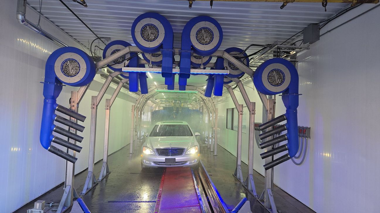 Car entering a car wash tunnel with blue brushes and water spraying inside.