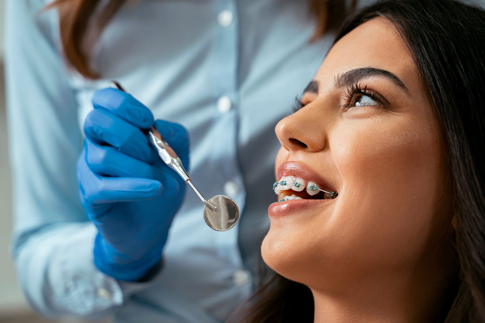 A woman with braces at a dental checkup, smiling while a dentist is holding a dental mirror.