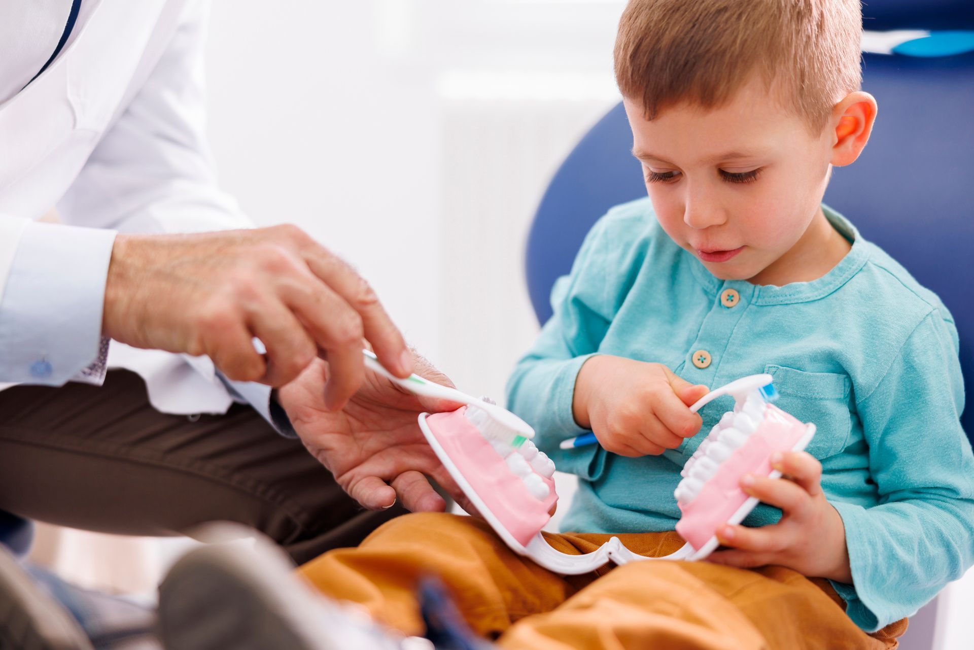 A dentist demonstrating teeth brushing to a little boy.