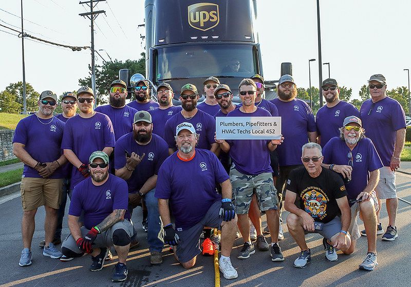 Group of UPS employees in purple shirts, smiling, standing in front of a UPS truck.