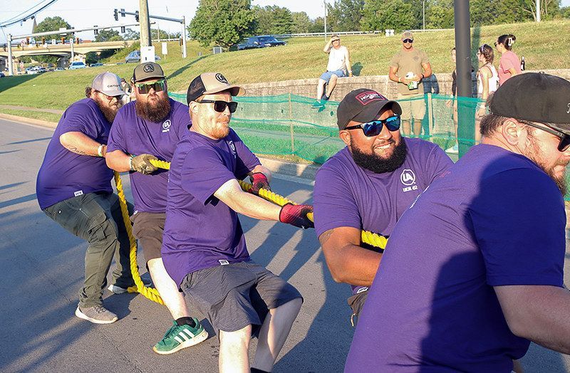 Men in purple shirts pulling a rope in a tug-of-war competition.