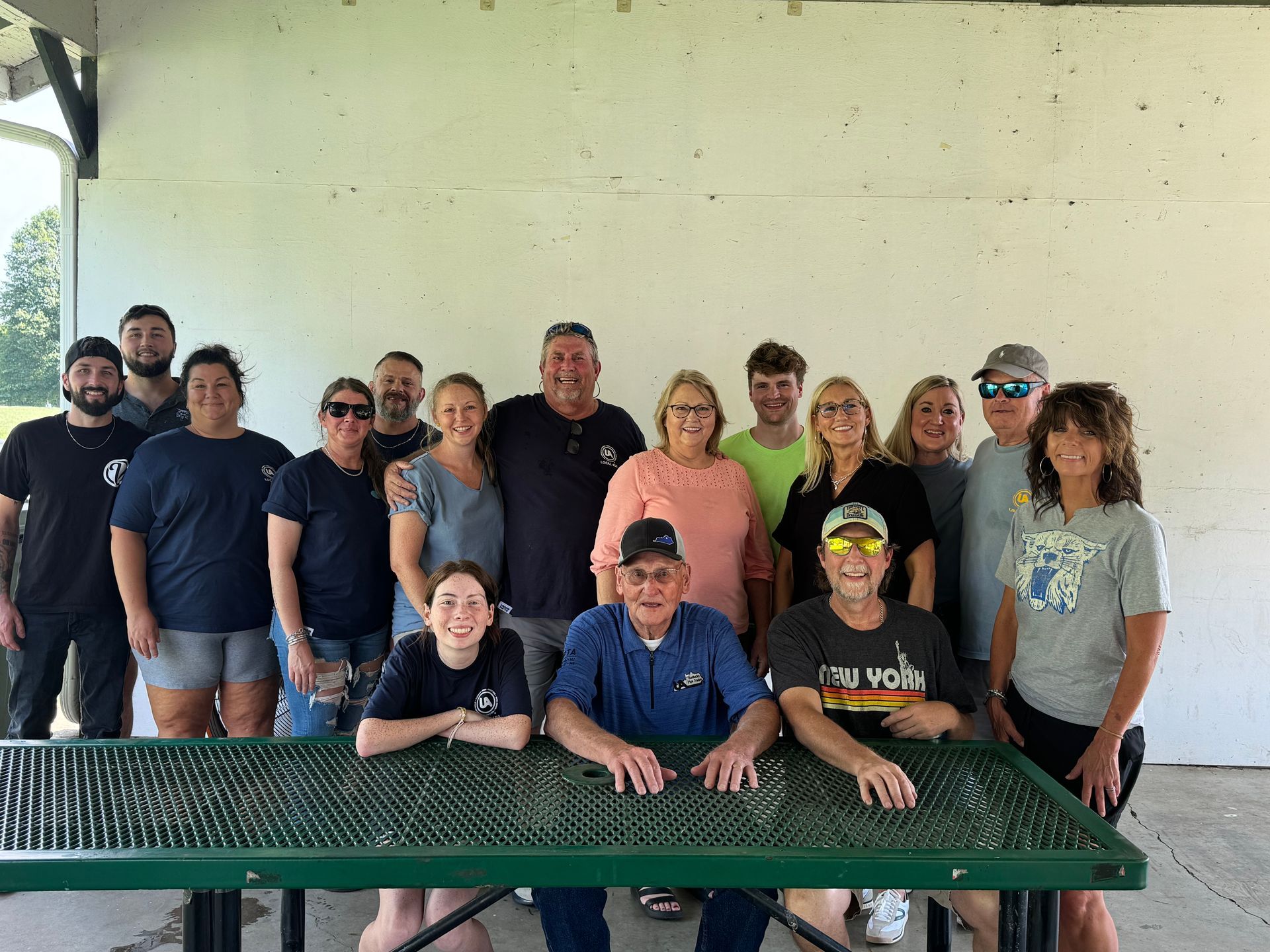 A group of people are posing for a picture at a picnic table.