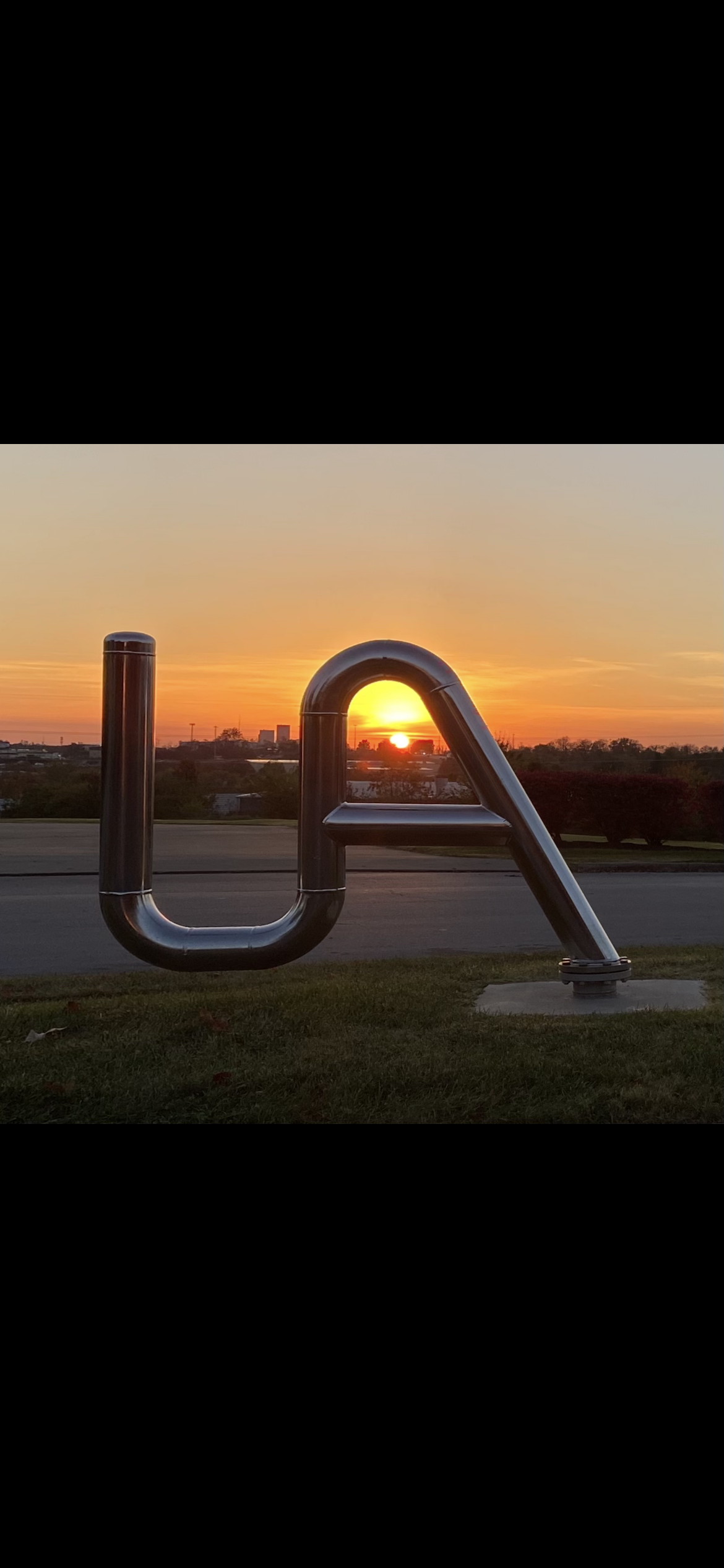 A large metal sculpture of the letter a with a sunset in the background.