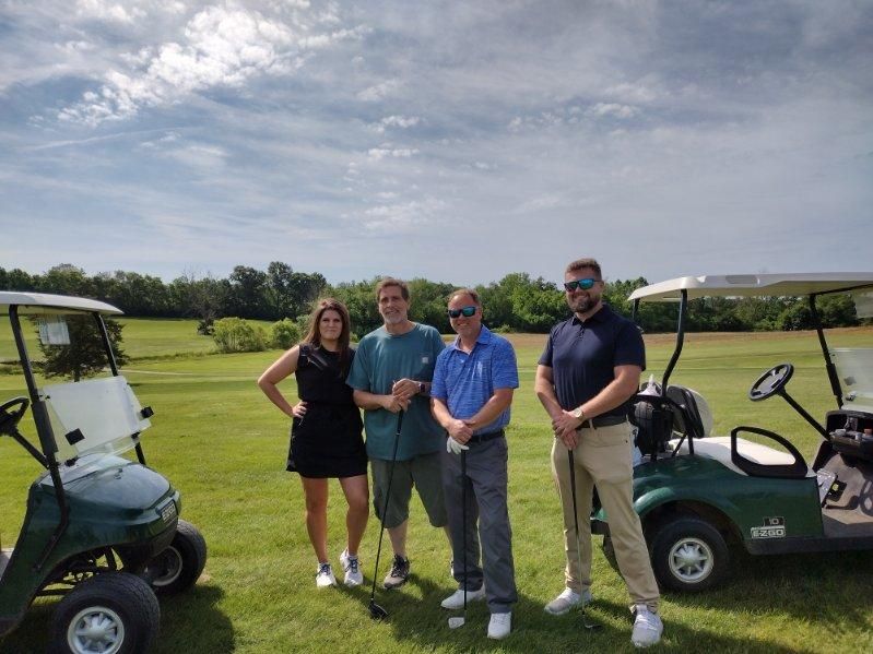 A group of people standing next to golf carts on a golf course.