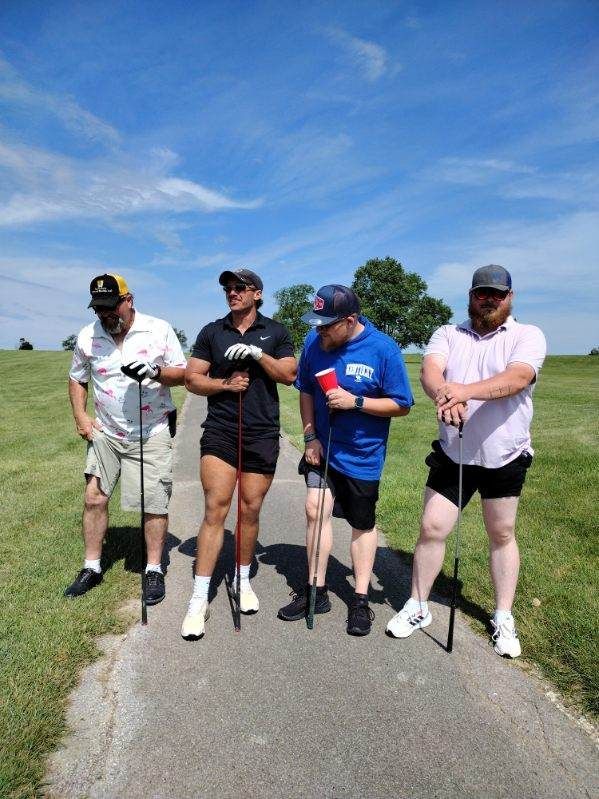A group of people are standing on a path holding golf clubs.