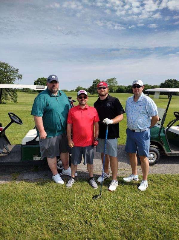 A group of men are standing in front of a golf cart on a golf course.