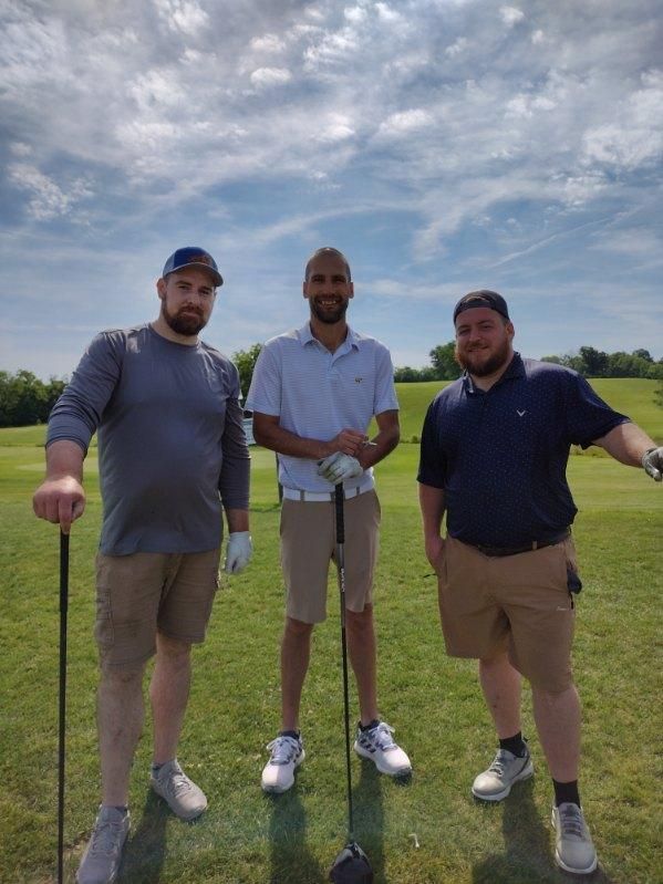 Three men are standing on a golf course holding golf clubs